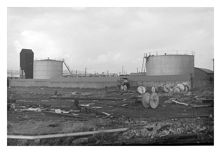mid-1950's to early 1960's - A photograph of the oil storage tanks situated at the Ferry Road side of the River Ely Tidal Harbour. A view from outside the perimeter security wall and fence.