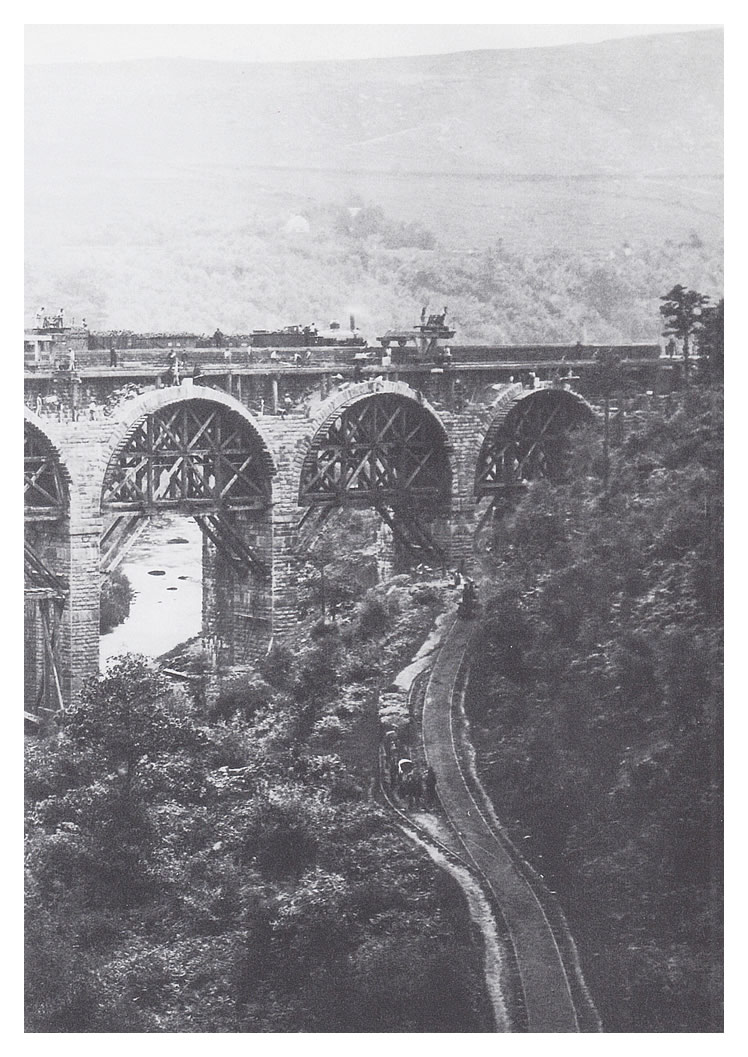 The Penydarren tramway still in use in 1862 with a southbound train hauled by two horses waiting in a turn-out. Construction goes on overhead on the Taff Vale Railway viaduct.